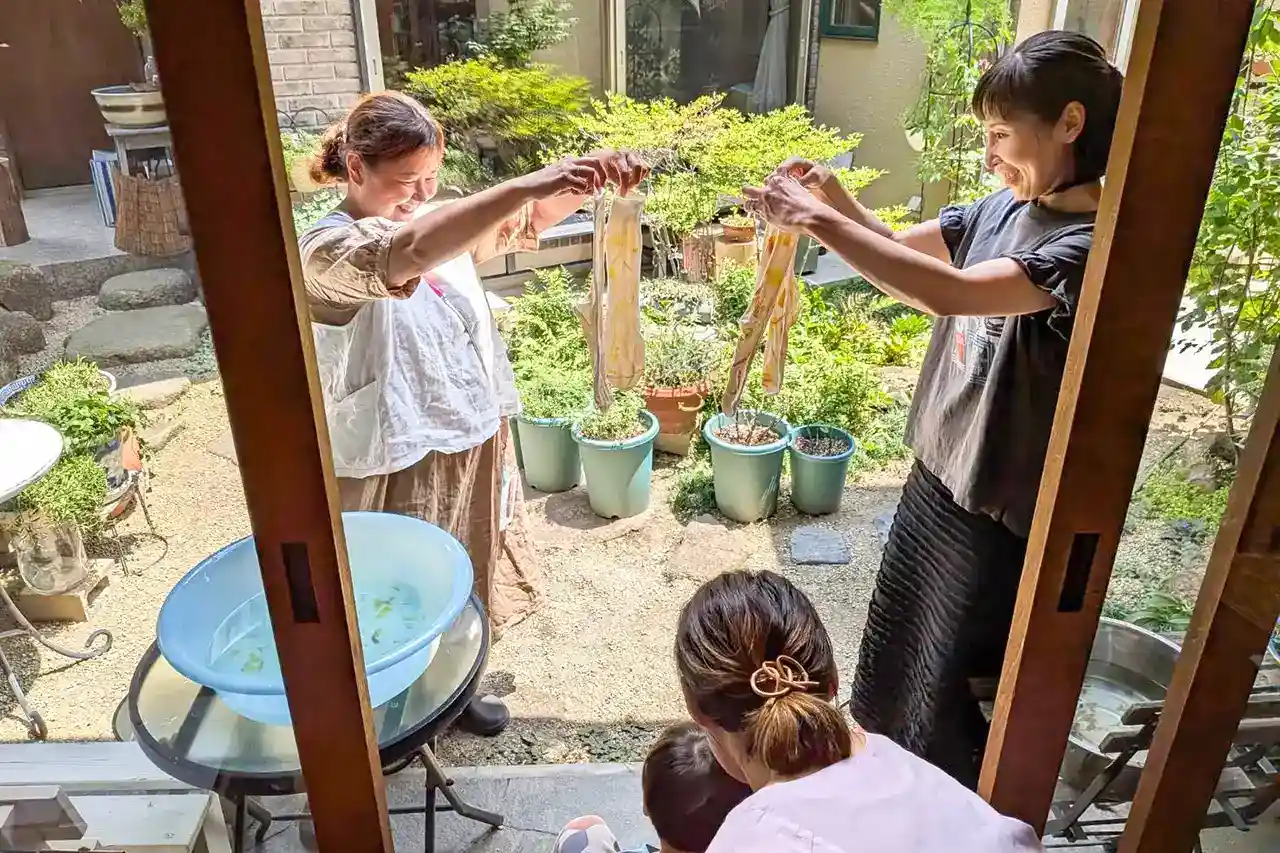 中庭で草木染めの作品を笑顔で見せ合う女性たち
